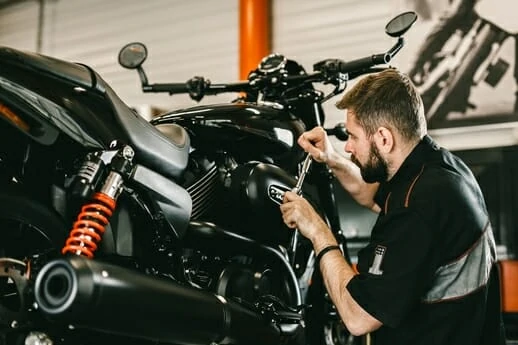 An image of a mechanic working on a black motorcycle with orange shocks. 