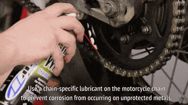 A mechanic oiling a motorcycle chain. 