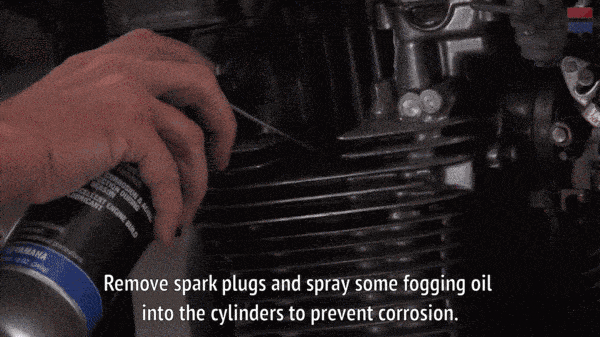 A mechanic spraying fogging oil into a motorcycle's cylinders.