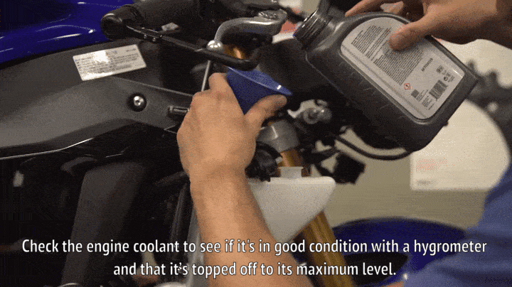 A mechanic topping of a motorcycle's coolant.
